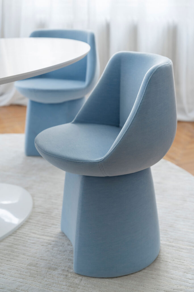 Sancal Magnumblauer Stuhl, modernes Design, minimalistischer Raum, eleganter Innenraum, organische Form, komfortabler Stuhl, Stoffbezug, runder Tisch, helles Interieur, natürliche Beleuchtung, weiche Textur, minimalistisches Mobiliar, elegantes Raumdesign, Wohnzimmermöbel, skandinavischer Stil